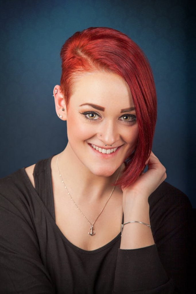 Studio portrait of a smiling woman with red hair and modern style.